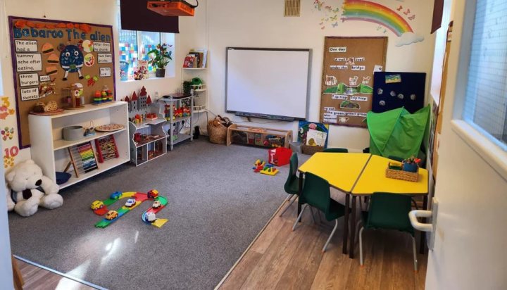Empty nursery classroom with a yellow table, toys and story displays.