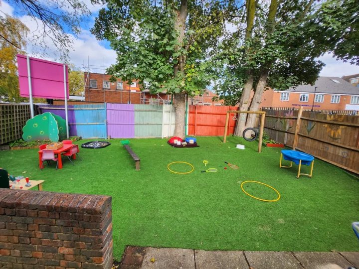 Fenced nursery garden with a tree, outdoor tables and play equipment.